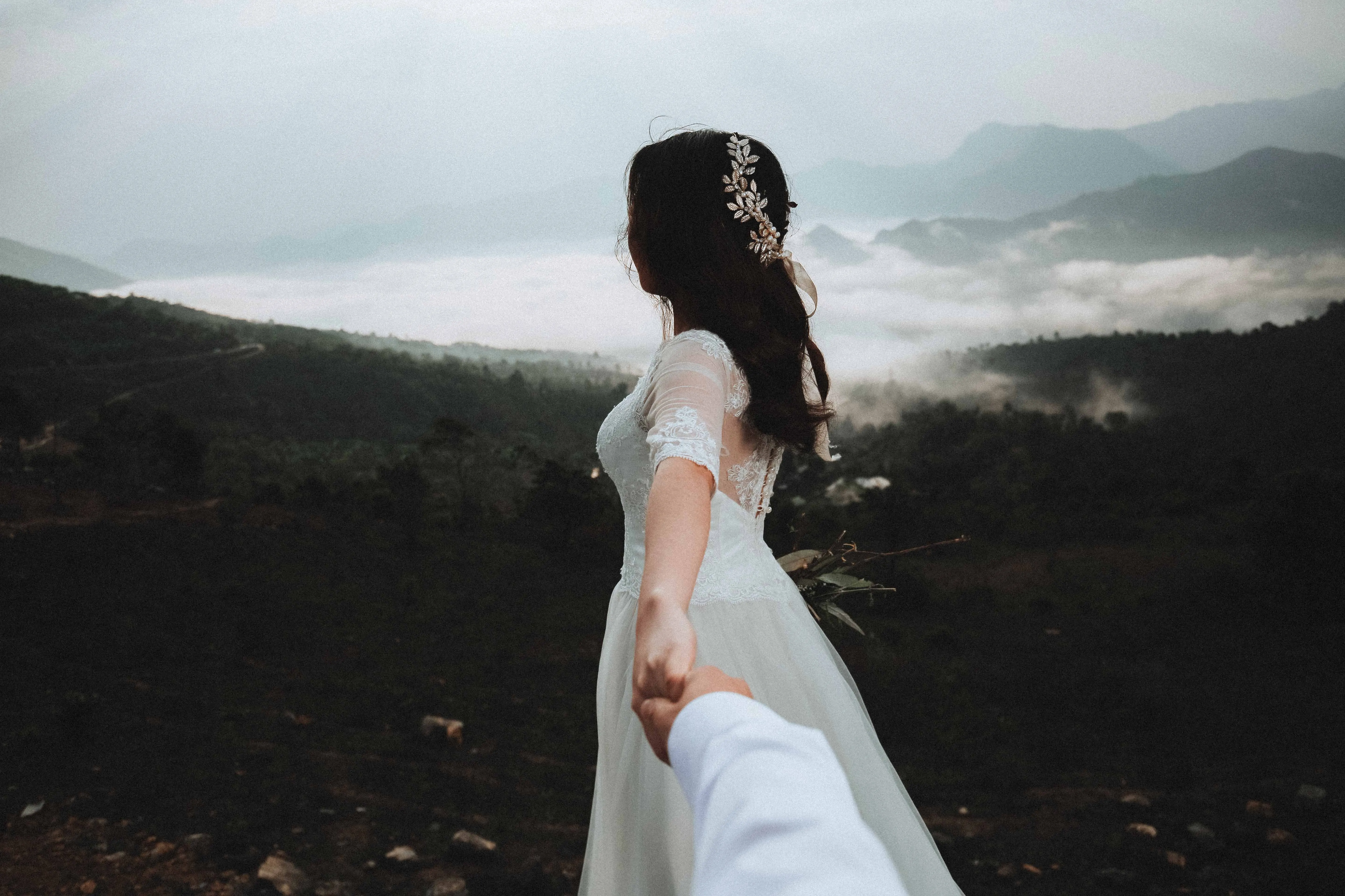 Point of view shot of a groom being led through mountaintops above the cloud-line by his bride.