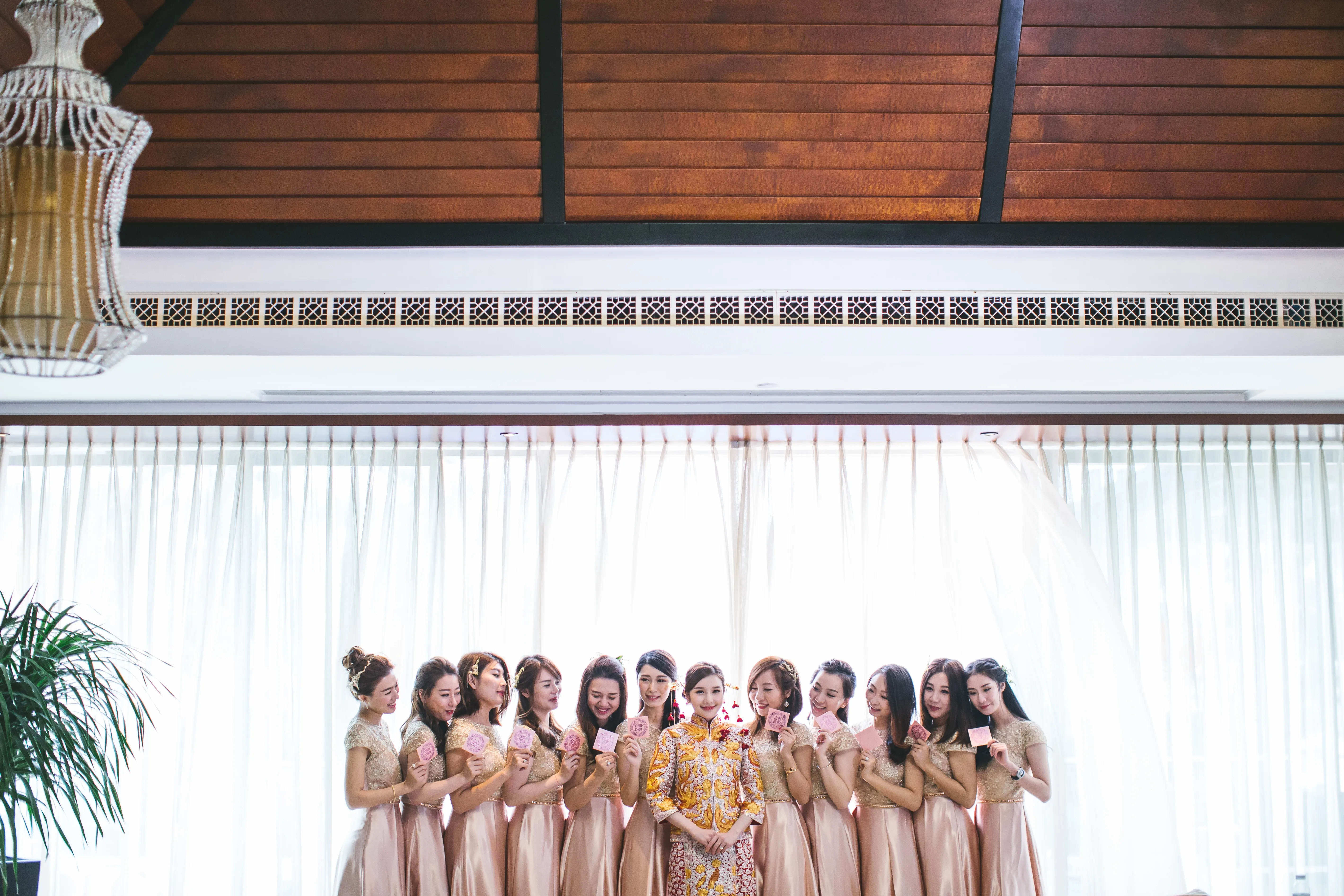 A bride in a pink Chinese style wedding dress embraced on both sides by her bride's-maids. 